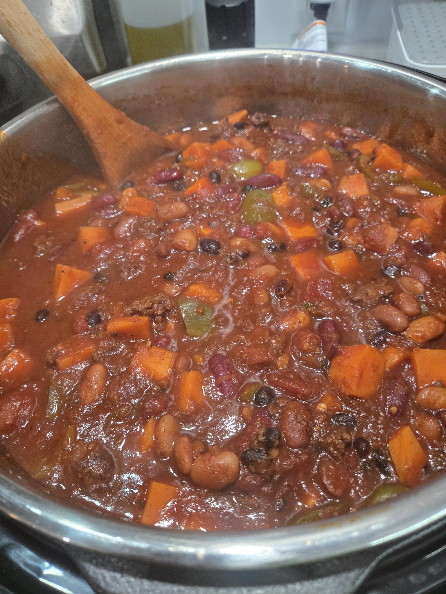 A closeup of the chili, chunks of bell pepper, sweet potato, and beans float in a deep red broth.
