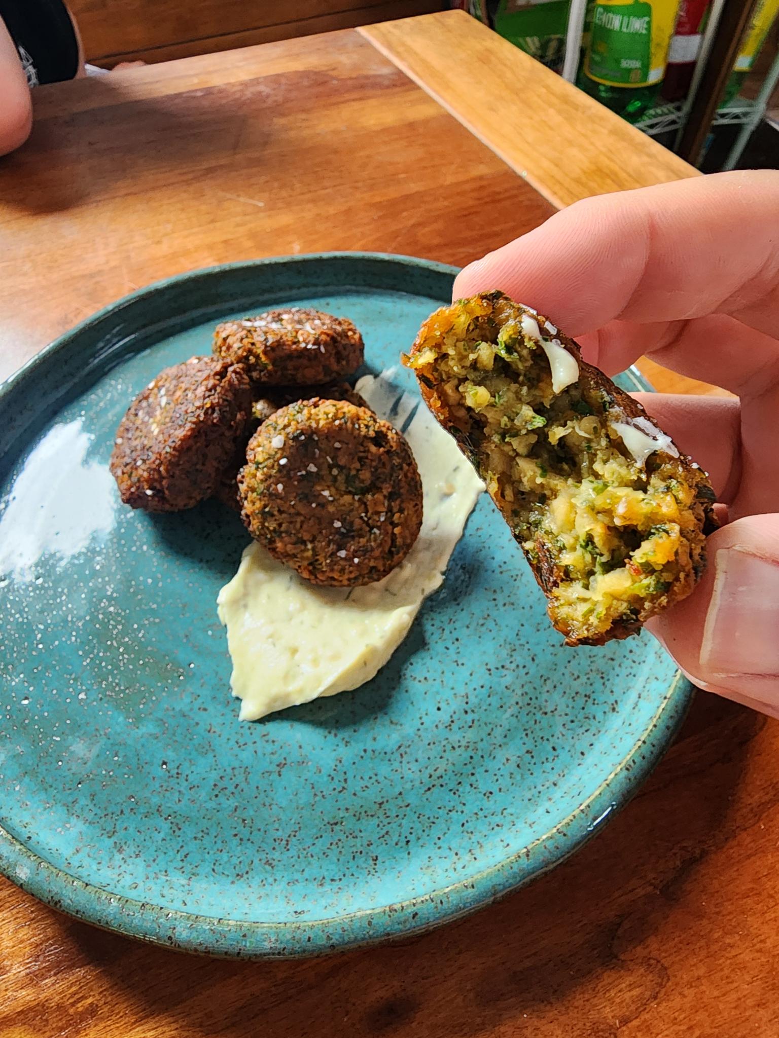 Falafel on a plate with a hand holding a bitten falafel in foreground